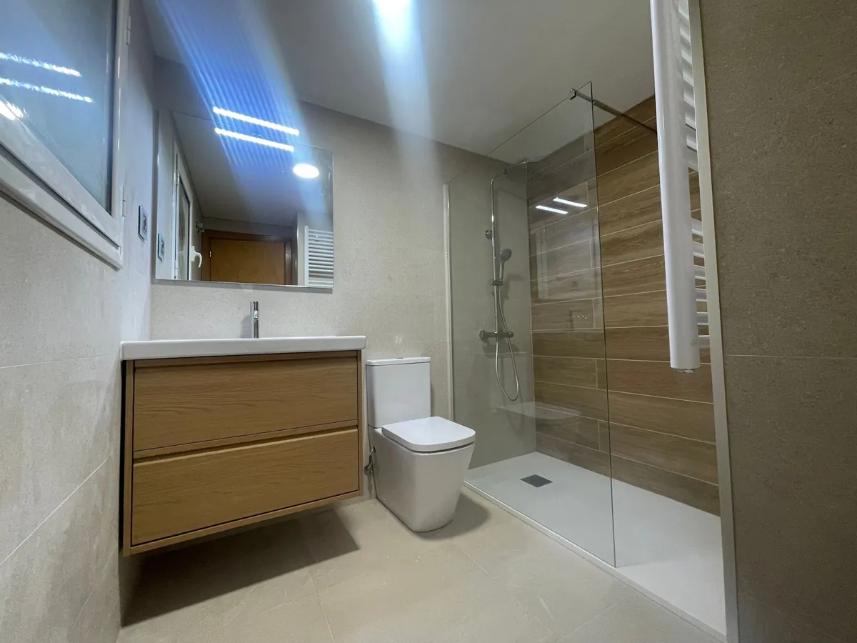 Baño con ducha a ras de suelo, mampara fija y mueble de madera